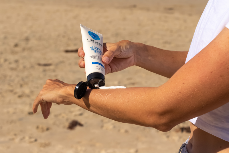 Person applying sunscreen to their arm on a sandy beach