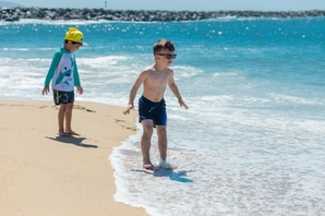 Two boys having fun on the beach wearing sun protection