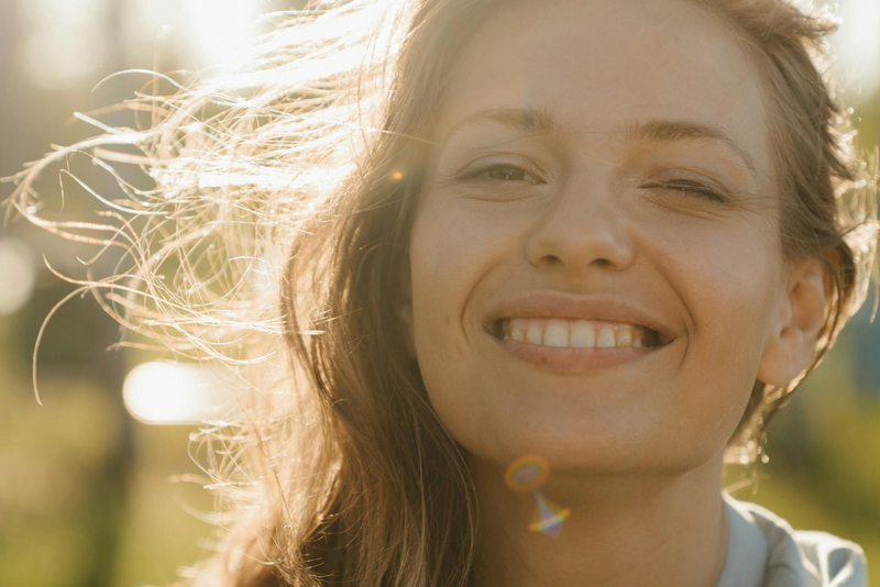 Smiling woman in sunlight with windblown hair and a natural, glowing expression