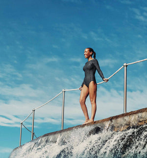 Model showcasing LITTLE URCHIN Natural Clear Zinc Sunscreen while standing near a waterfall